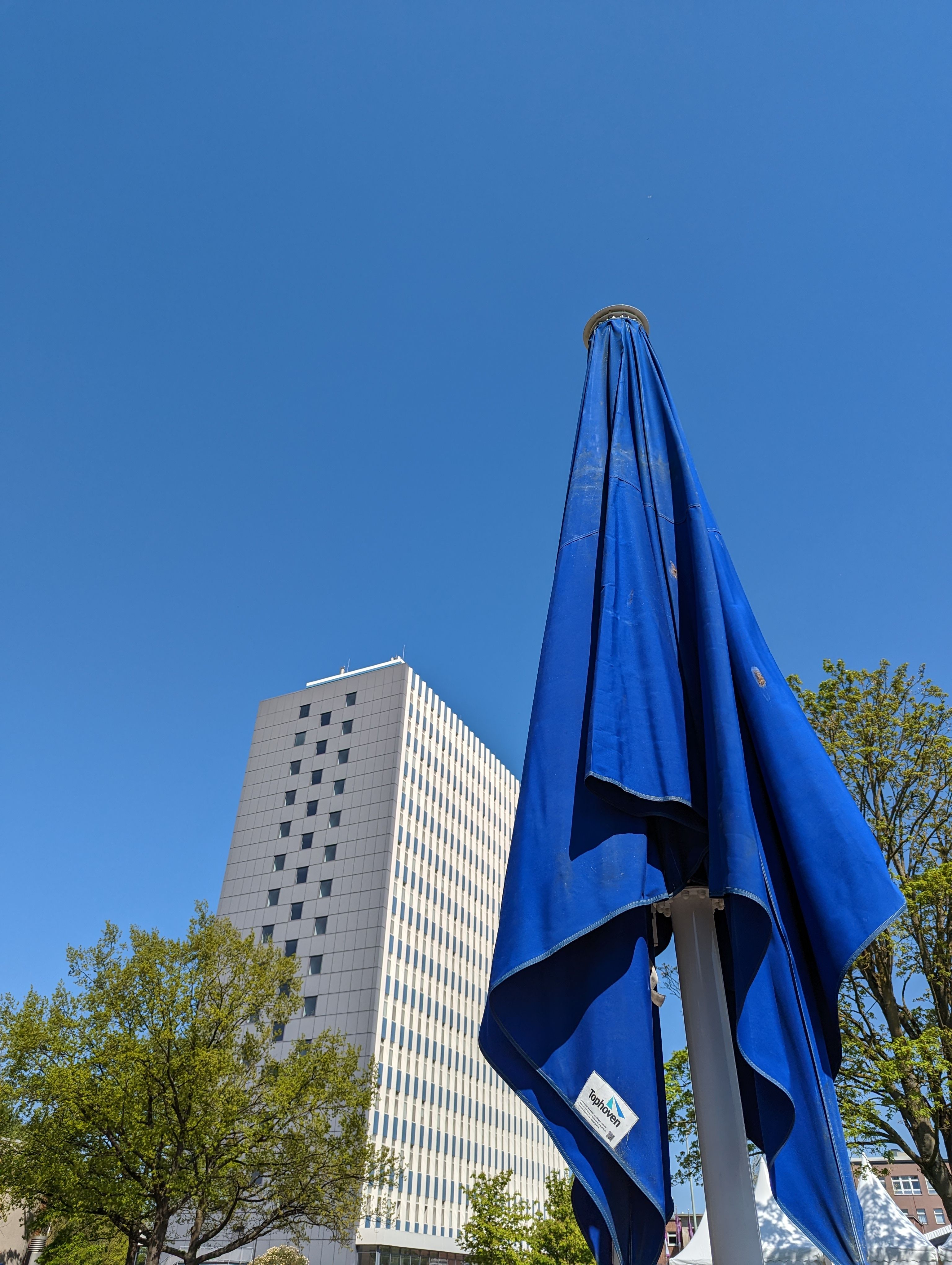 Der Blick auf das Uni-Hochhaus vorbei an einem blauen Sonnenschirm